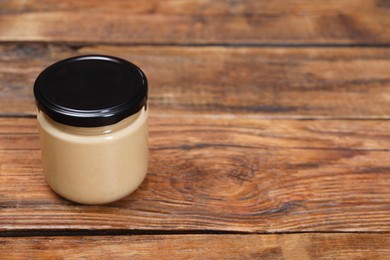 Photo of Tasty nut paste in jar on wooden table. Space for text