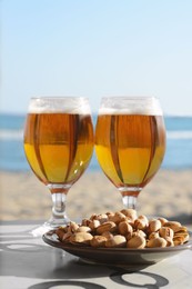 Glasses of cold beer and pistachios on table near sea