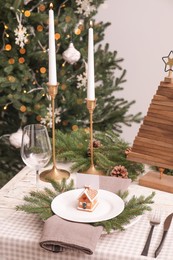 Festive place setting with beautiful dishware, cutlery and gingerbread house card holder for Christmas dinner on white wooden table