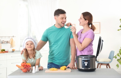 Photo of Happy family preparing food with modern multi cooker in kitchen