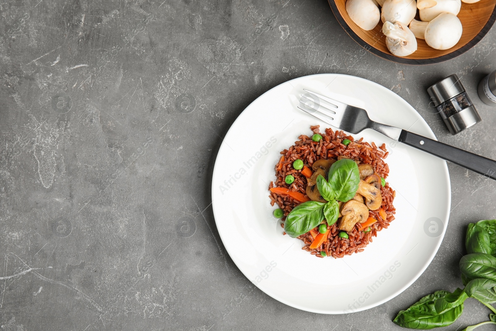 Photo of Plate of tasty brown rice with vegetables and mushrooms on grey table, flat lay. Space for text