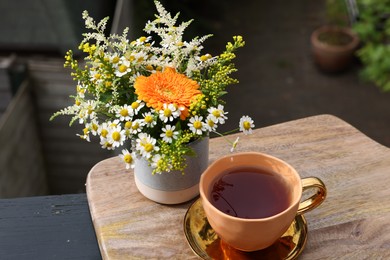 Photo of Cup of delicious chamomile tea and fresh flowers outdoors on sunny day