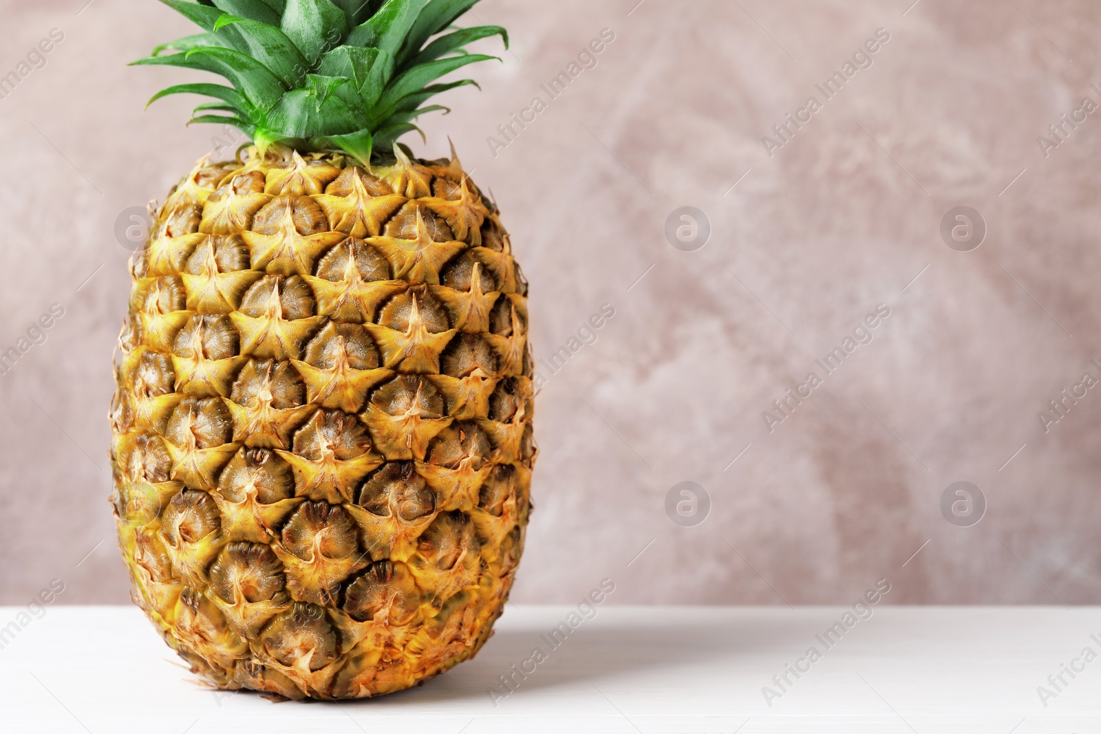 Photo of Delicious ripe pineapple on white table near pink wall, closeup. Space for text