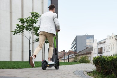 Photo of Businessman riding modern kick scooter on city street, back view. Space for text