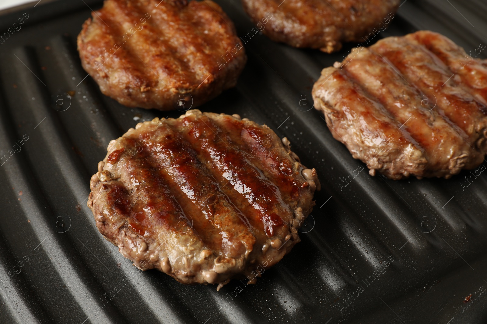 Photo of Delicious hamburger patties cooking on electric grill, closeup