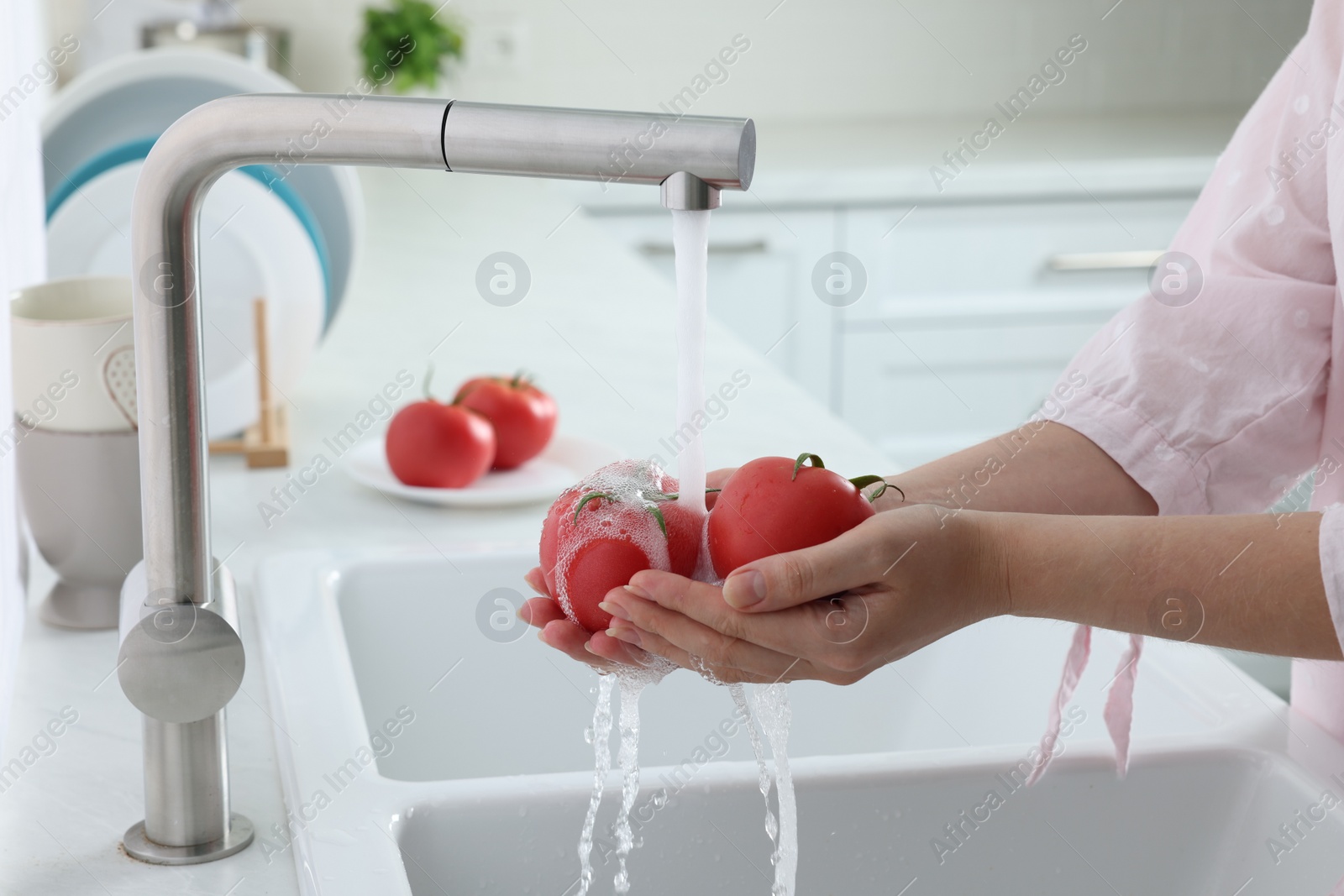 Photo of Woman washing fresh ripe tomatoes under tap water in kitchen, closeup