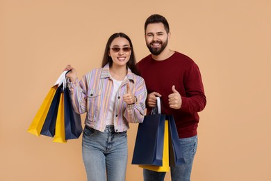Photo of Happy couple with shopping bags showing thumbs up on beige background