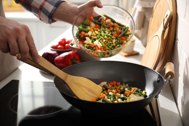 Photo of Man pouring mix of fresh vegetables into frying pan, closeup
