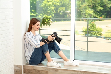 Photo of Professional photographer with modern camera sitting near window indoors