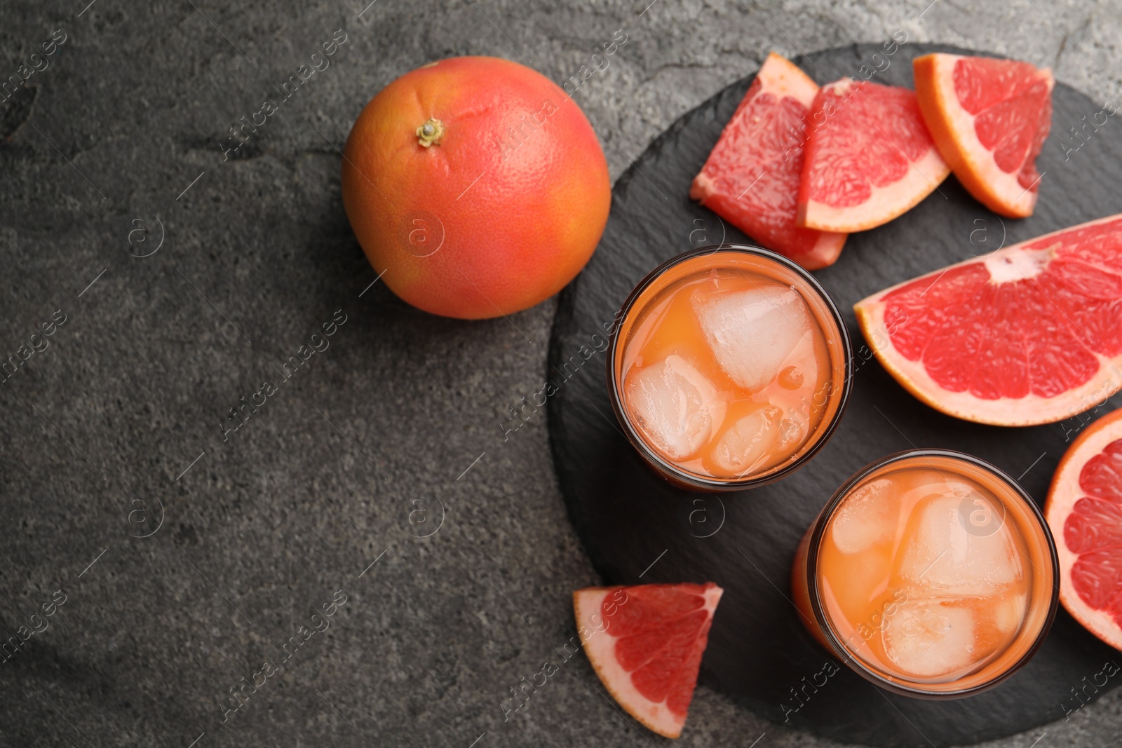 Photo of Tasty grapefruit drink with ice in glasses and fresh fruits on dark textured table, flat lay. Space for text