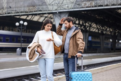 Being late. Worried couple with suitcase waiting at train station