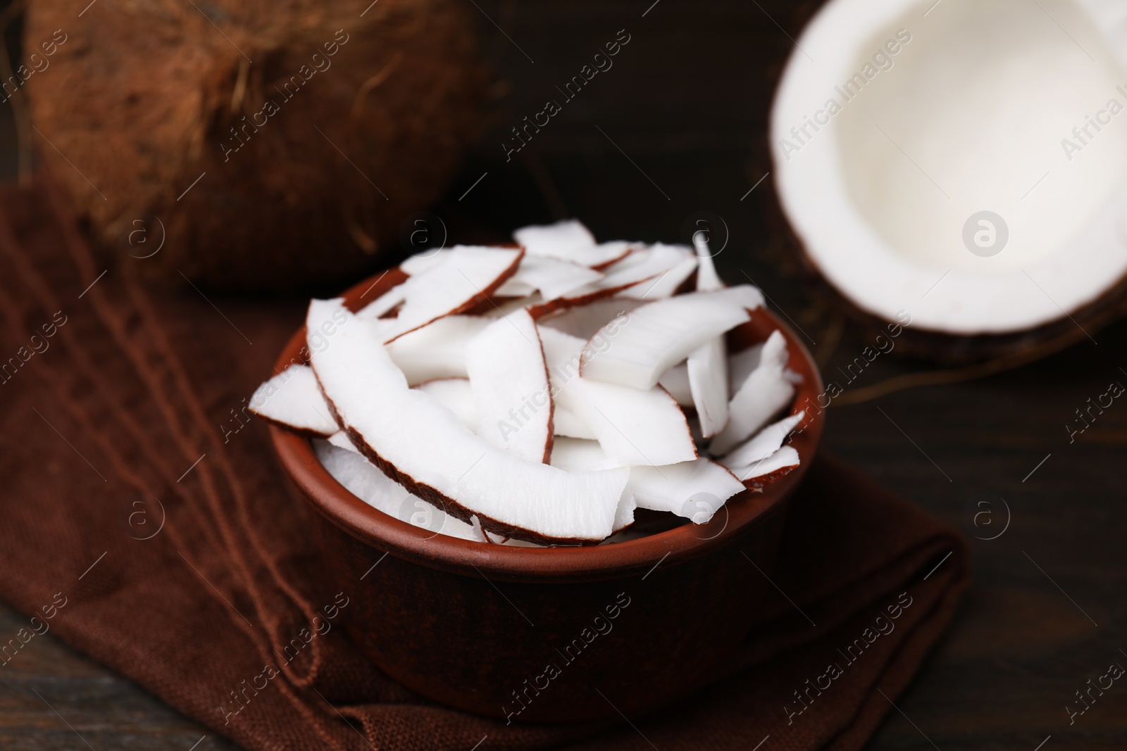 Photo of Coconut pieces in bowl and nuts on wooden table, closeup