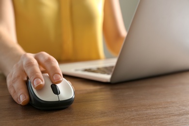 Woman using computer mouse with laptop at table, closeup