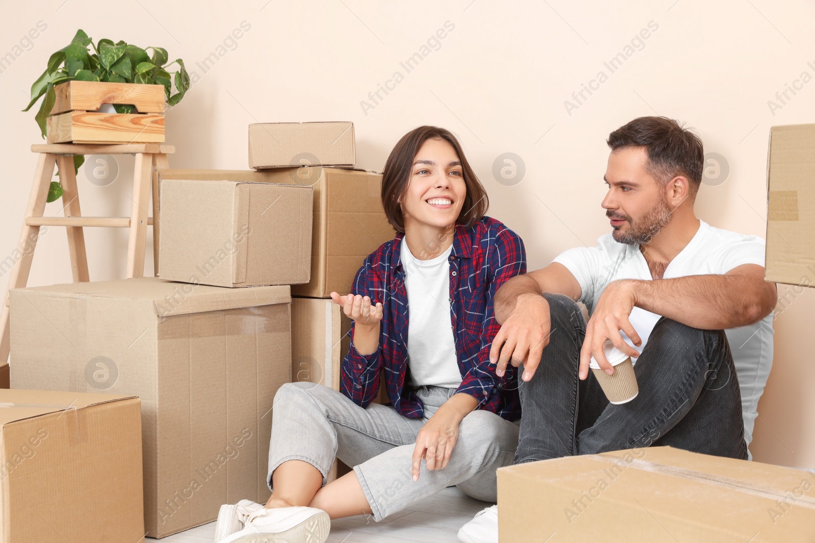 Photo of Happy couple with takeaway coffee resting on floor in new apartment. Moving day