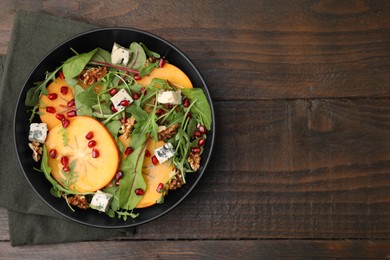 Photo of Tasty salad with persimmon, blue cheese, pomegranate and walnuts served on wooden table, top view. Space for text