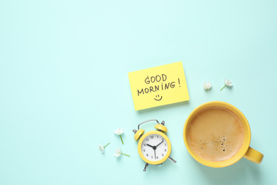 Photo of Delicious coffee, alarm clock and card with GOOD MORNING wish on light blue background, flat lay. Space for text