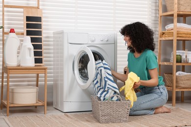 Happy woman putting laundry into washing machine indoors