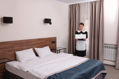 Photo of Beautiful chambermaid with stack of fresh towels in hotel room