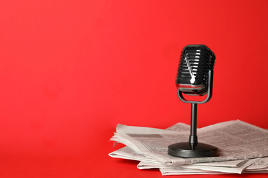 Newspapers and vintage microphone on red background, space for text. Journalist's work