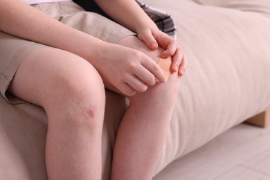 Photo of Little boy putting sticking plaster onto knee on sofa, closeup. Space for text