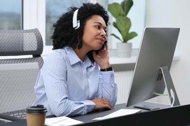Photo of Young woman with headphones working on computer in office
