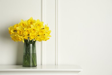 Photo of Beautiful daffodils in vase on table near white wall indoors, space for text