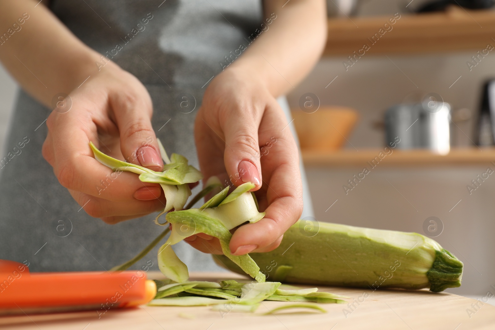 Photo of Woman with peels of fresh zucchini at table in kitchen, closeup. Space for text