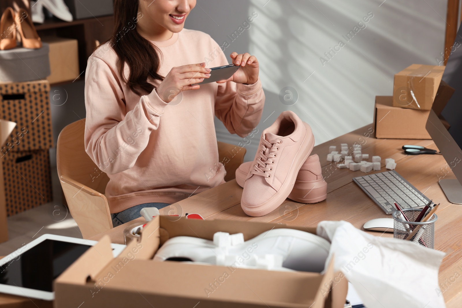 Photo of Shoes seller taking picture of pink sneakers at table in office, closeup. Online store