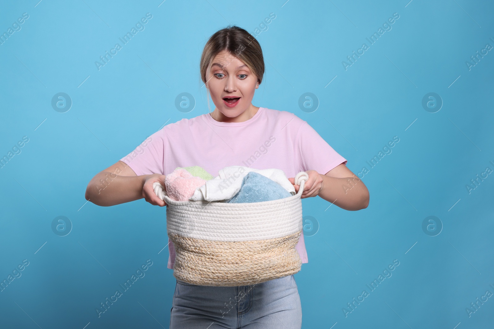 Photo of Emotional woman with basket full of laundry on light blue background