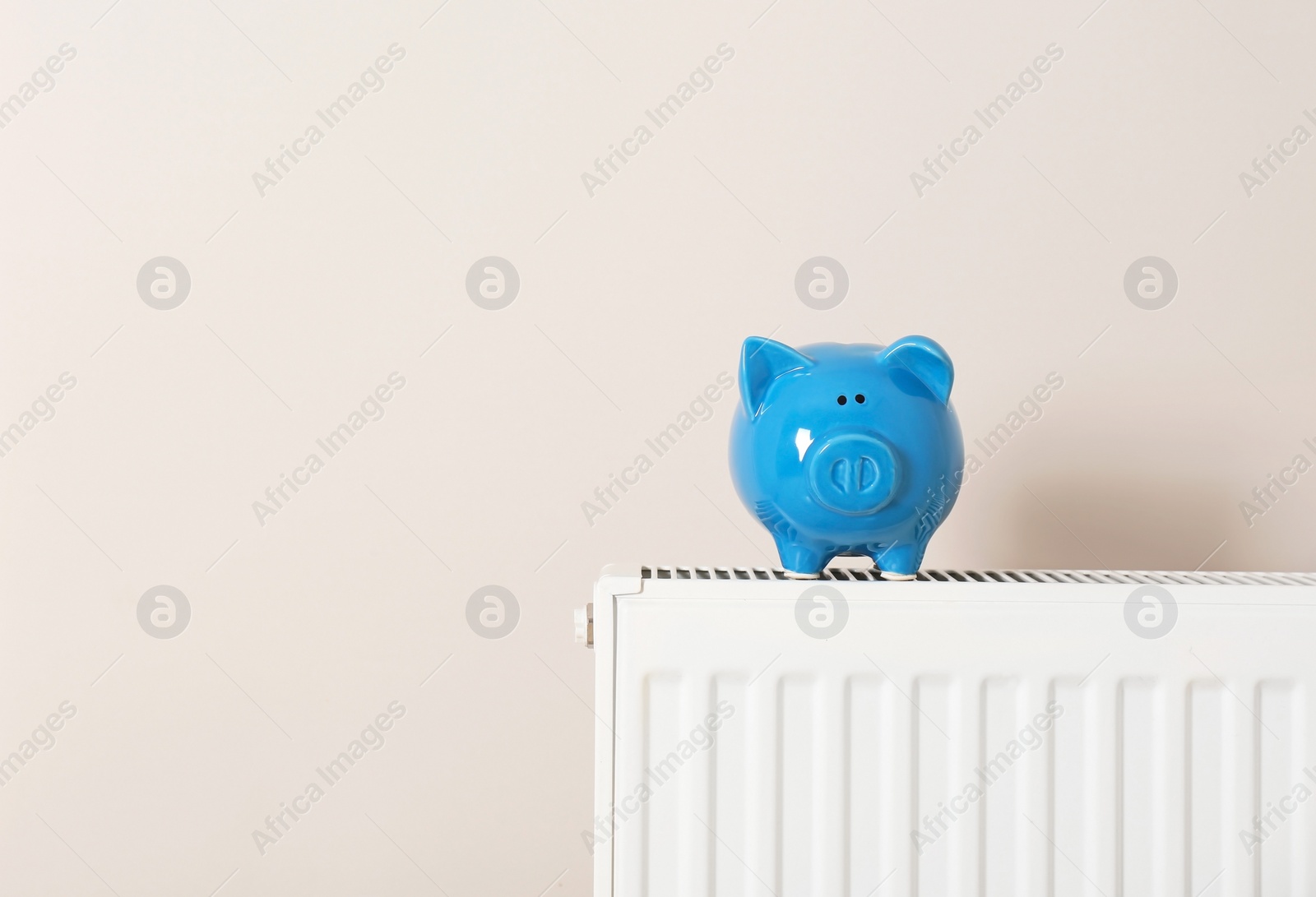 Photo of Piggy bank on heating radiator against light background. Space for text