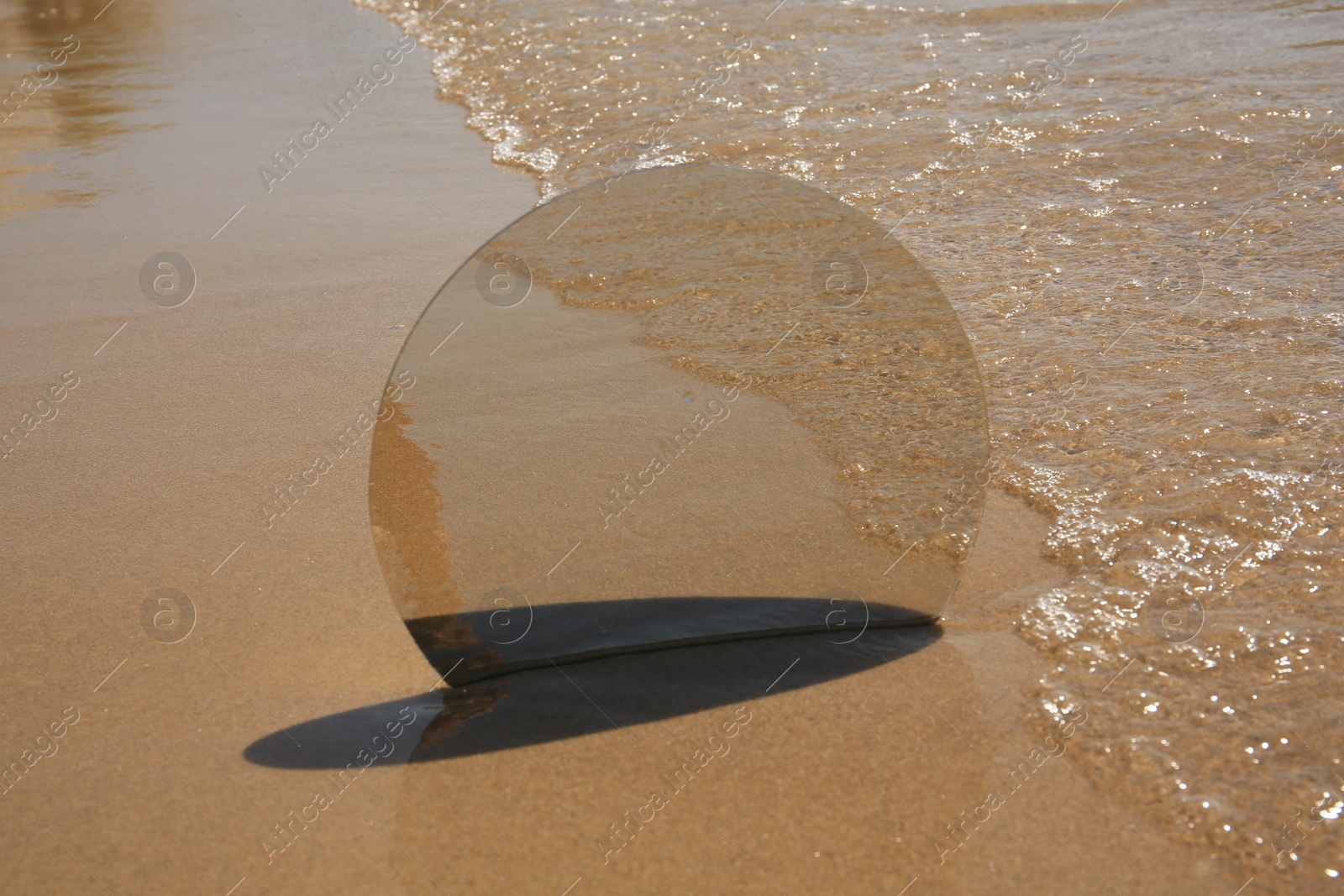 Photo of Round mirror reflecting sea on sandy beach