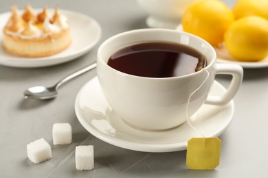 Tea bag in ceramic cup of hot water and sugar on grey table