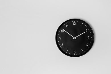 Stylish analog clock hanging on light wall. Space for text