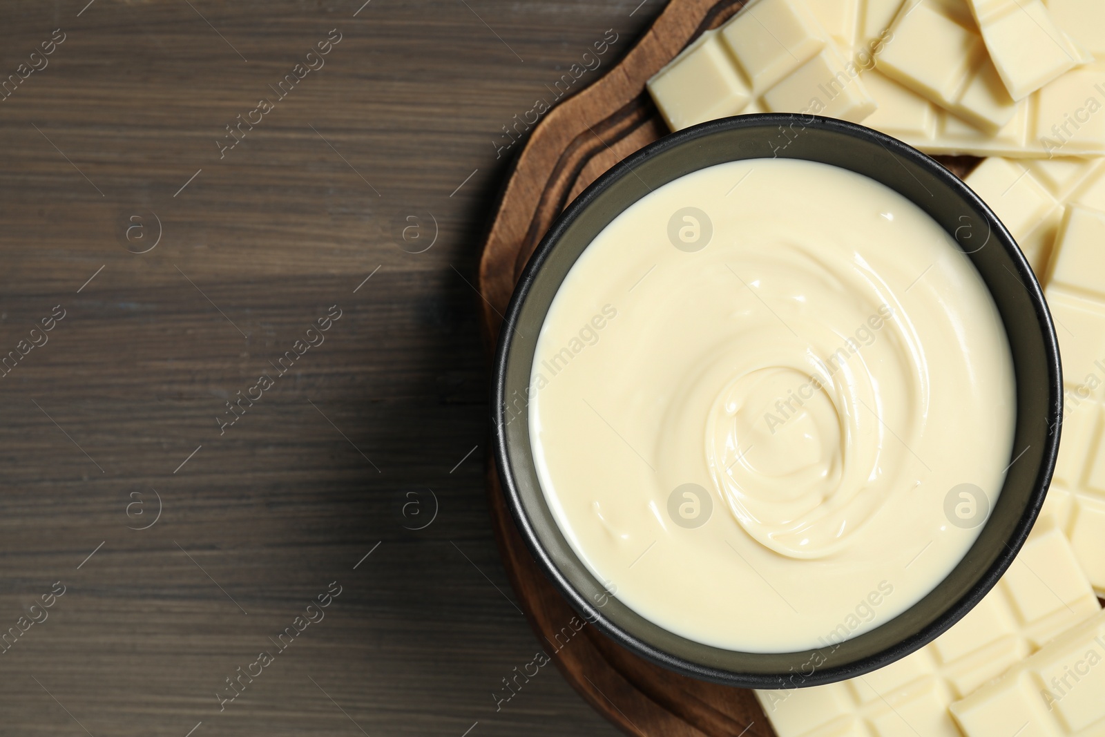 Photo of Tasty white chocolate paste in bowl and pieces on wooden table, top view. Space for text
