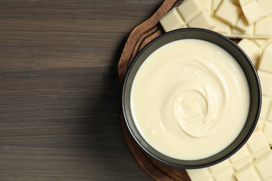 Photo of Tasty white chocolate paste in bowl and pieces on wooden table, top view. Space for text