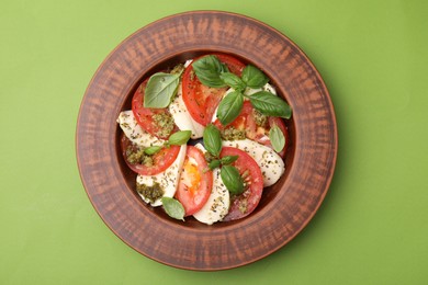Photo of Plate of delicious Caprese salad with pesto sauce on green table, top view