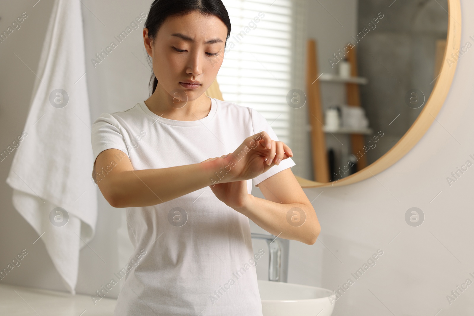 Photo of Suffering from allergy. Young woman scratching her arm in bathroom