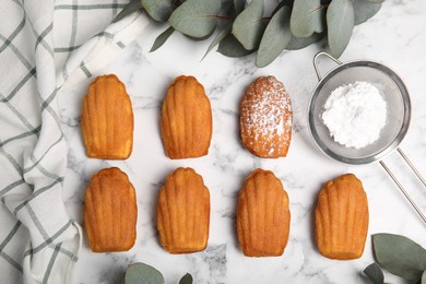 Photo of Delicious madeleine cakes and powdered sugar on white marble table, flat lay