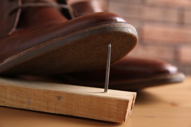 Metal nail in wooden plank and shoes on table, closeup