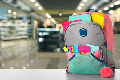 Image of Bright backpack with school stationery on table in shopping mall. Space for text