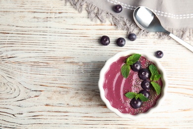 Flat lay composition with bowl of tasty acai smoothie on wooden table