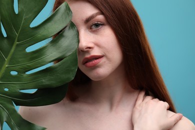 Photo of Beautiful woman with freckles and monstera leaf on light blue background, closeup