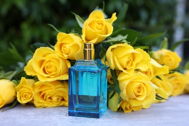 Perfume and beautiful bouquet of yellow roses on light table outdoors