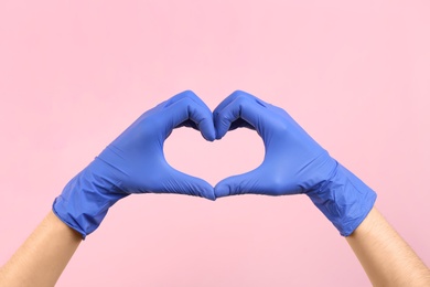 Person in medical gloves showing heart gesture on pink background, closeup of hands