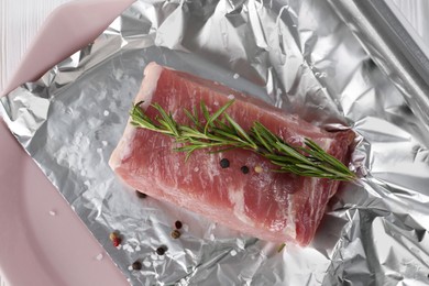 Photo of Aluminum foil with raw meat, rosemary and spices on white table, top view
