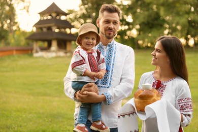 Photo of Happy cute family in embroidered Ukrainian shirts with korovai bread on sunny day. Space for text