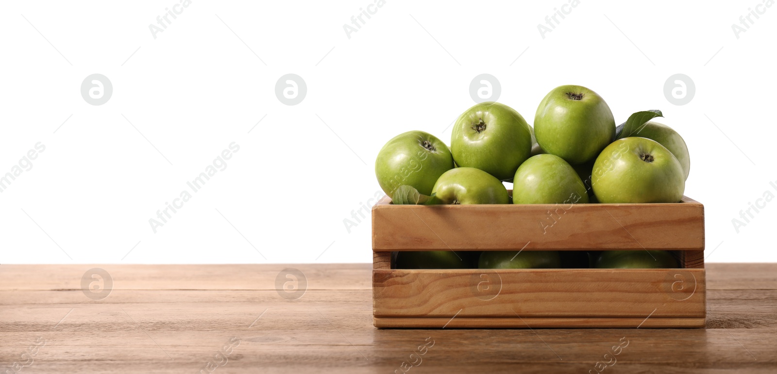 Photo of Ripe green apples in crate on wooden table against white background. Space for text