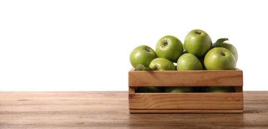 Photo of Ripe green apples in crate on wooden table against white background. Space for text