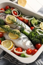 Raw fish with vegetables and lemon in baking dish on table