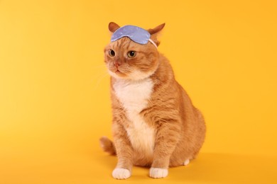 Cute ginger cat with sleep mask on orange background